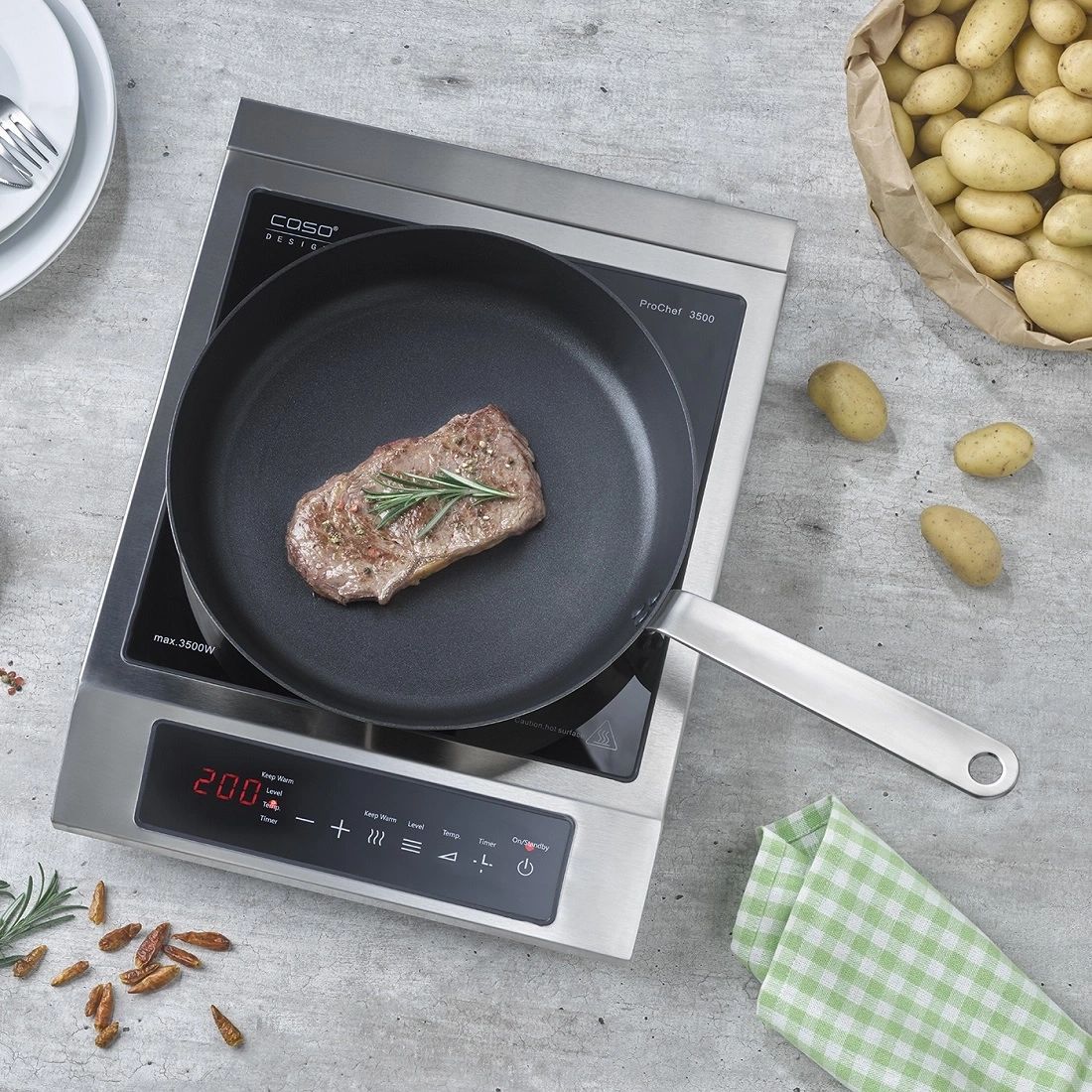 Steak in pan on induction cooktop with potatoes and herbs, cooking scene