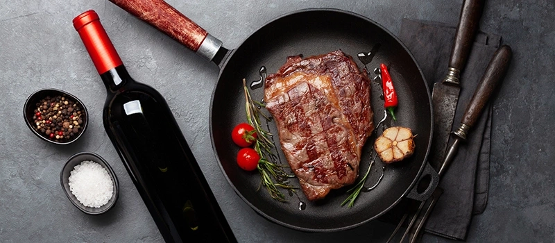 Grilled steak with wine, spices, and vegetables on a table setting.