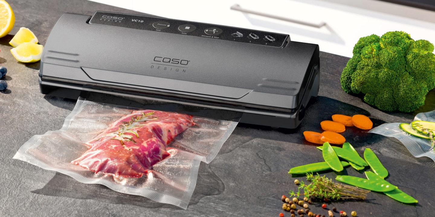 Vacuum sealer with meat and vegetables on a dark surface, ready to be sealed.
