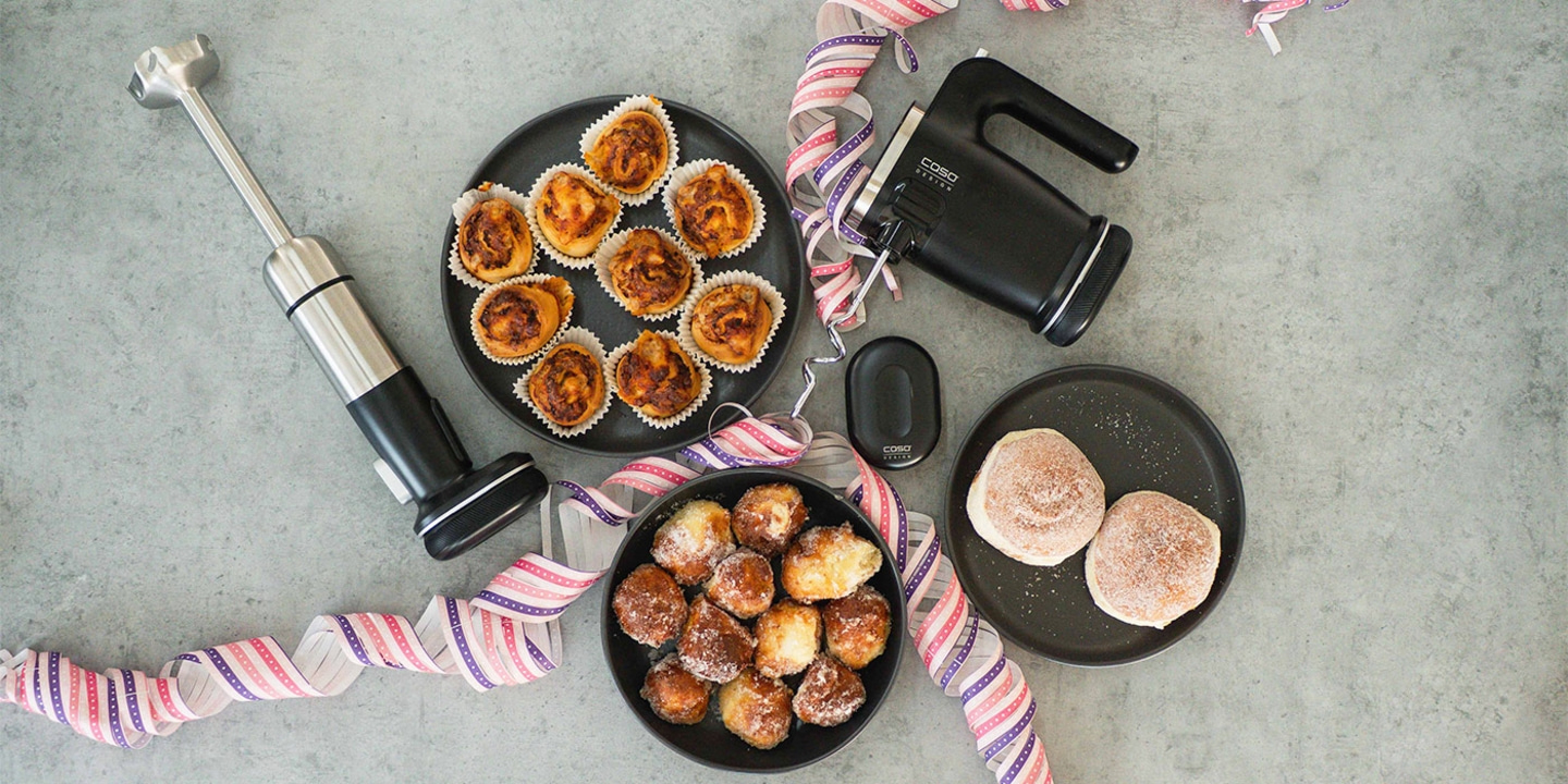 Three plates of pastries, a mixer, and decorations on a gray surface.