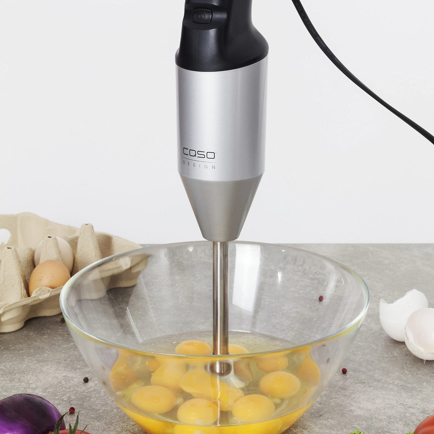 Handmixer in einer Glasschüssel mit Eiern, die gerade verquirlt werden.