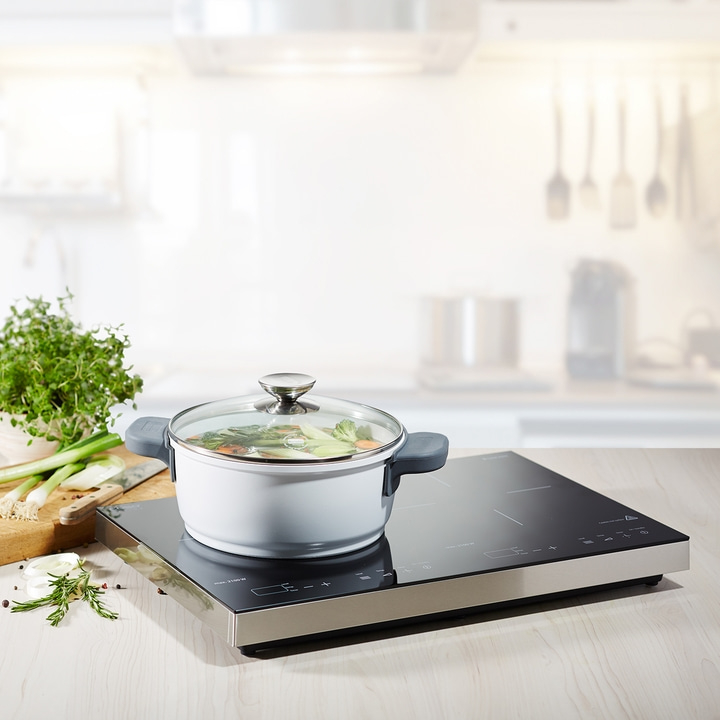 Pot with vegetables on induction cooktop in kitchen with herbs and ingredients
