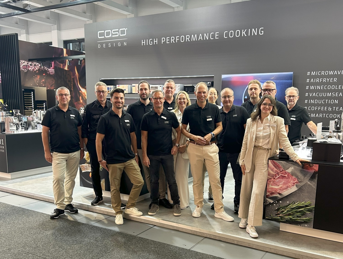 Gruppe von Personen posiert vor einem Stand mit dem Logo 'COSO DESIGN'.