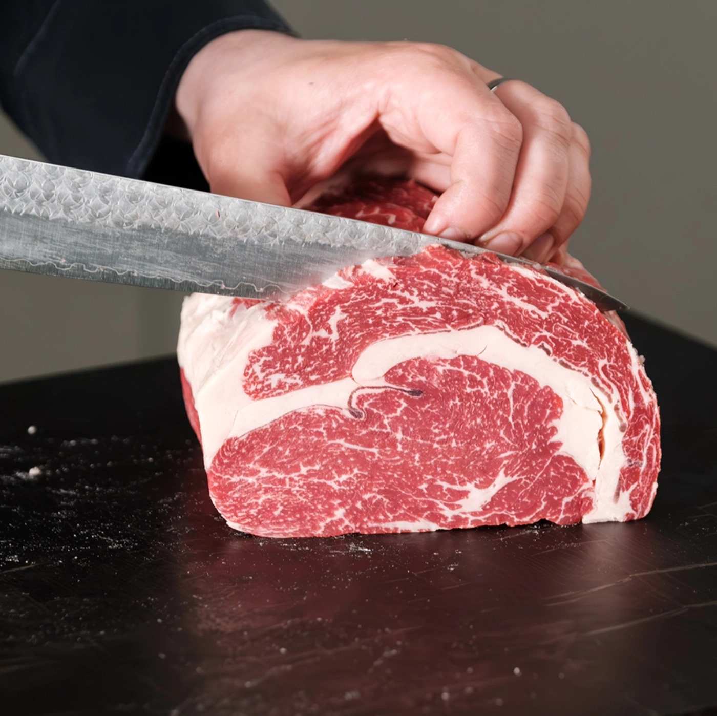 A butcher cuts a raw piece of meat with a lot of fat and marbling.