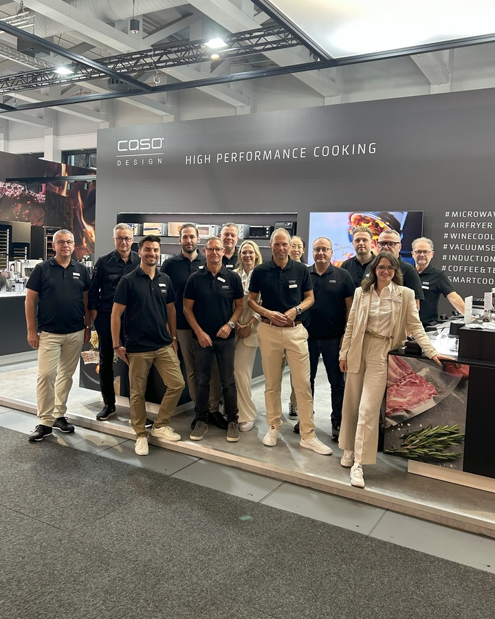 Gruppe von Personen posiert vor einem Stand mit Küchengeräten.