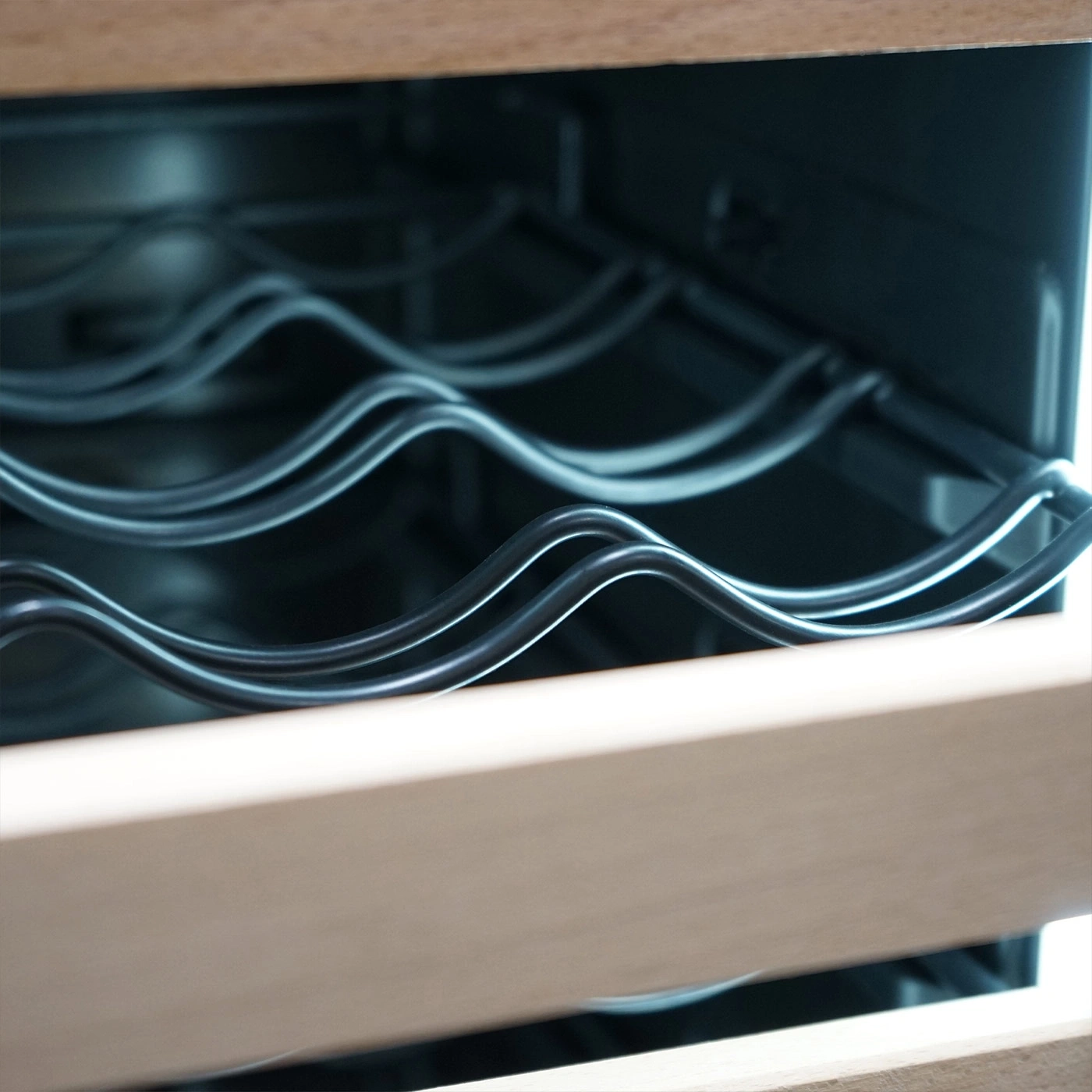 Close-up of a wine fridge with wavy wire racks and wooden frame