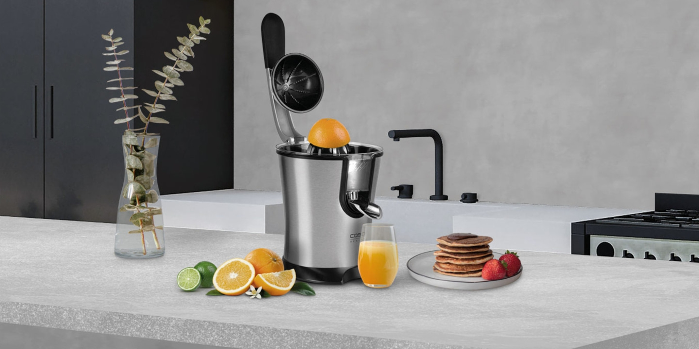 Küchenszene mit Saftpresse, Obst, Saft und Pfannkuchen