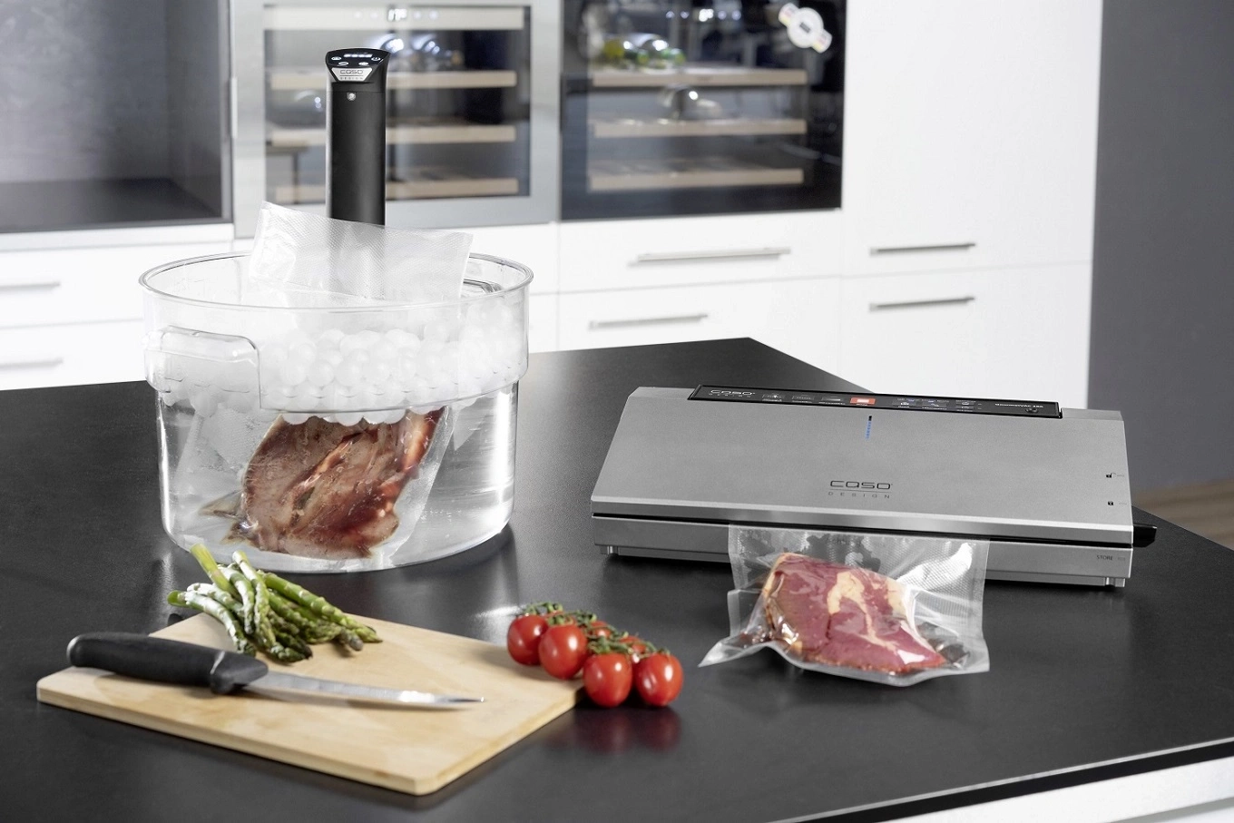 Sous-Vide-Gerät mit Fleisch, Gemüse und Vakuumierer auf einer Arbeitsplatte