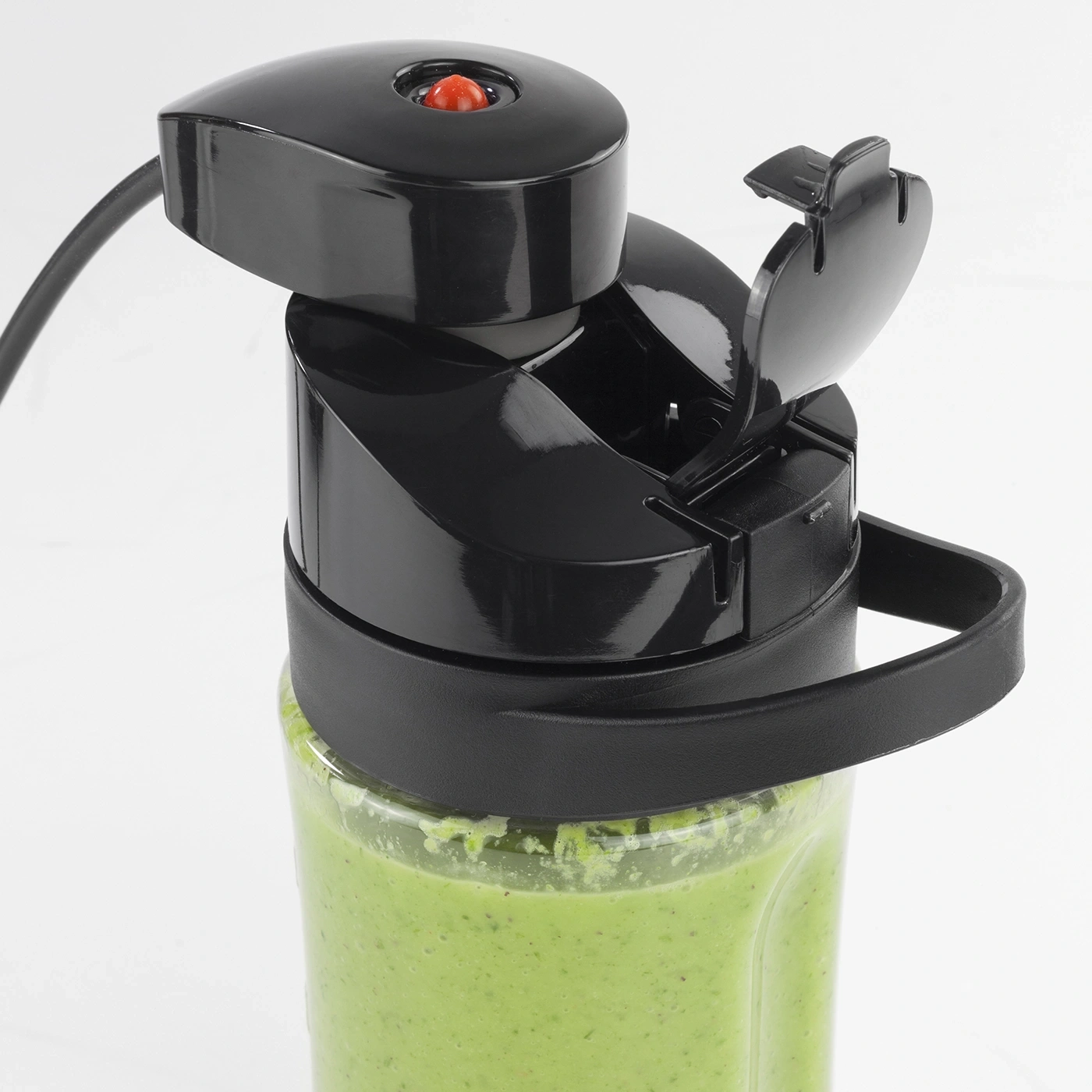 Black blender with red button and green contents, close-up, open lid, handle visible