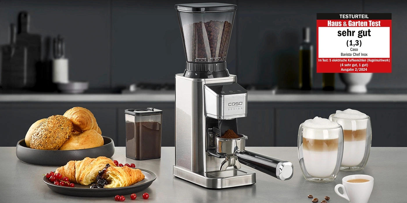 Kaffeemühle mit Zubehör und Testurteil 'sehr gut' auf einem Tisch mit Essen.