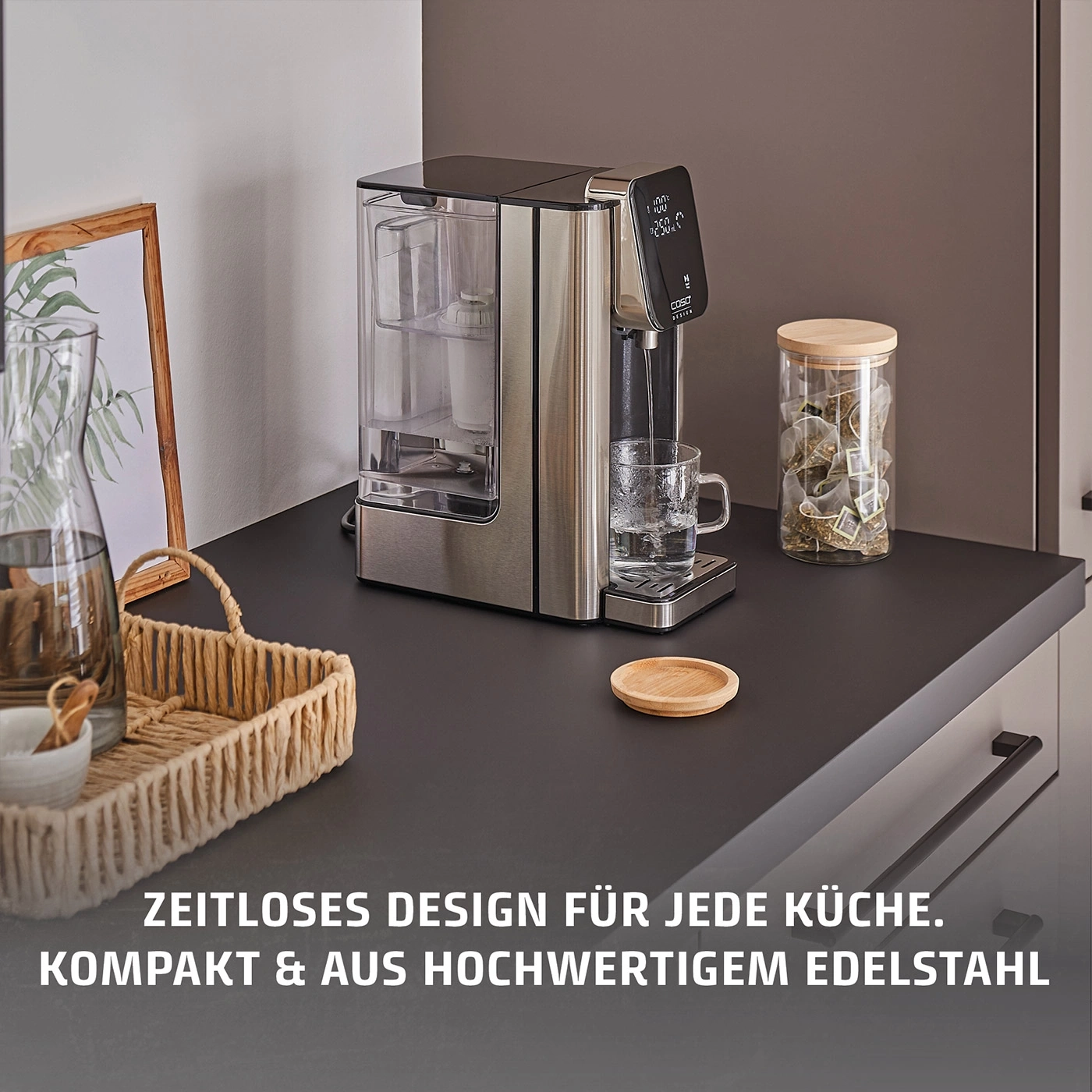 Ein Wasserspender mit digitalem Display und ein Glas mit Teebeuteln auf einer Arbeitsplatte.
