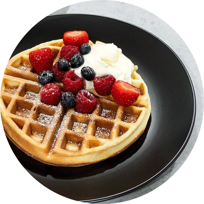 Waffel mit Beeren und Sahne auf einem schwarzen Teller, Nahaufnahme