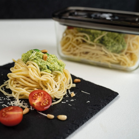 Spaghetti with pesto, tomatoes, and pine nuts served on a black slate.