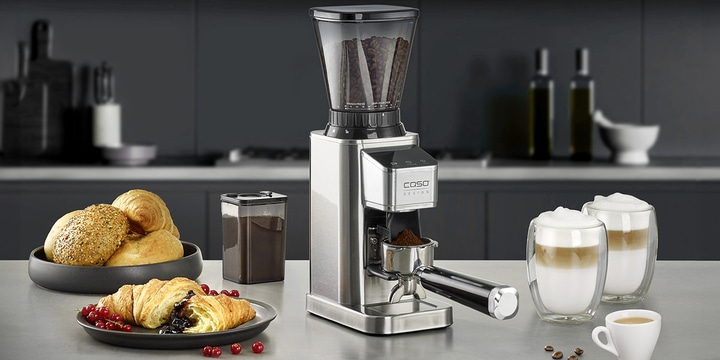 Coffee grinder with coffee, croissants and latte macchiato on the table.