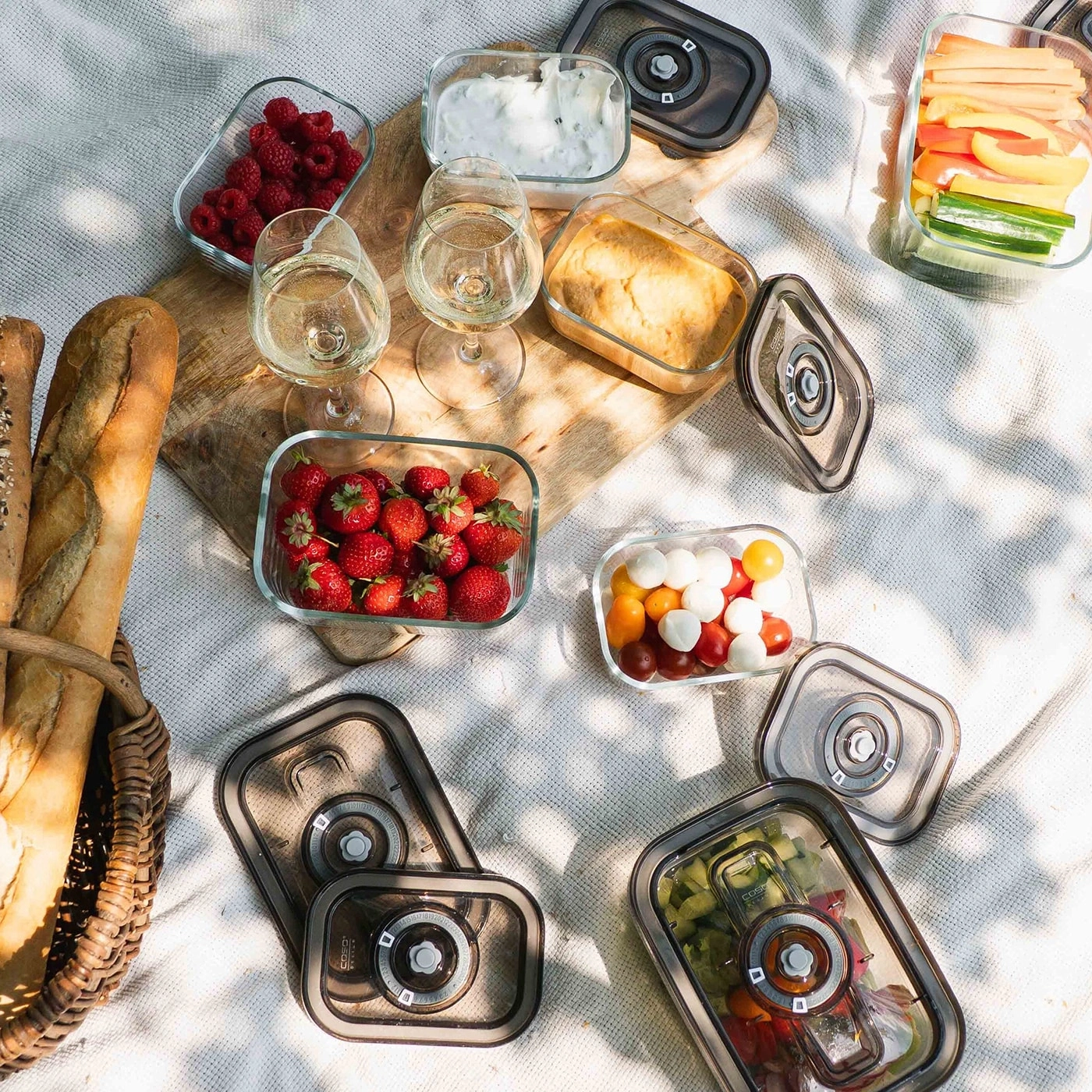 Picnic with food, drinks, and containers on an outdoor blanket setting.