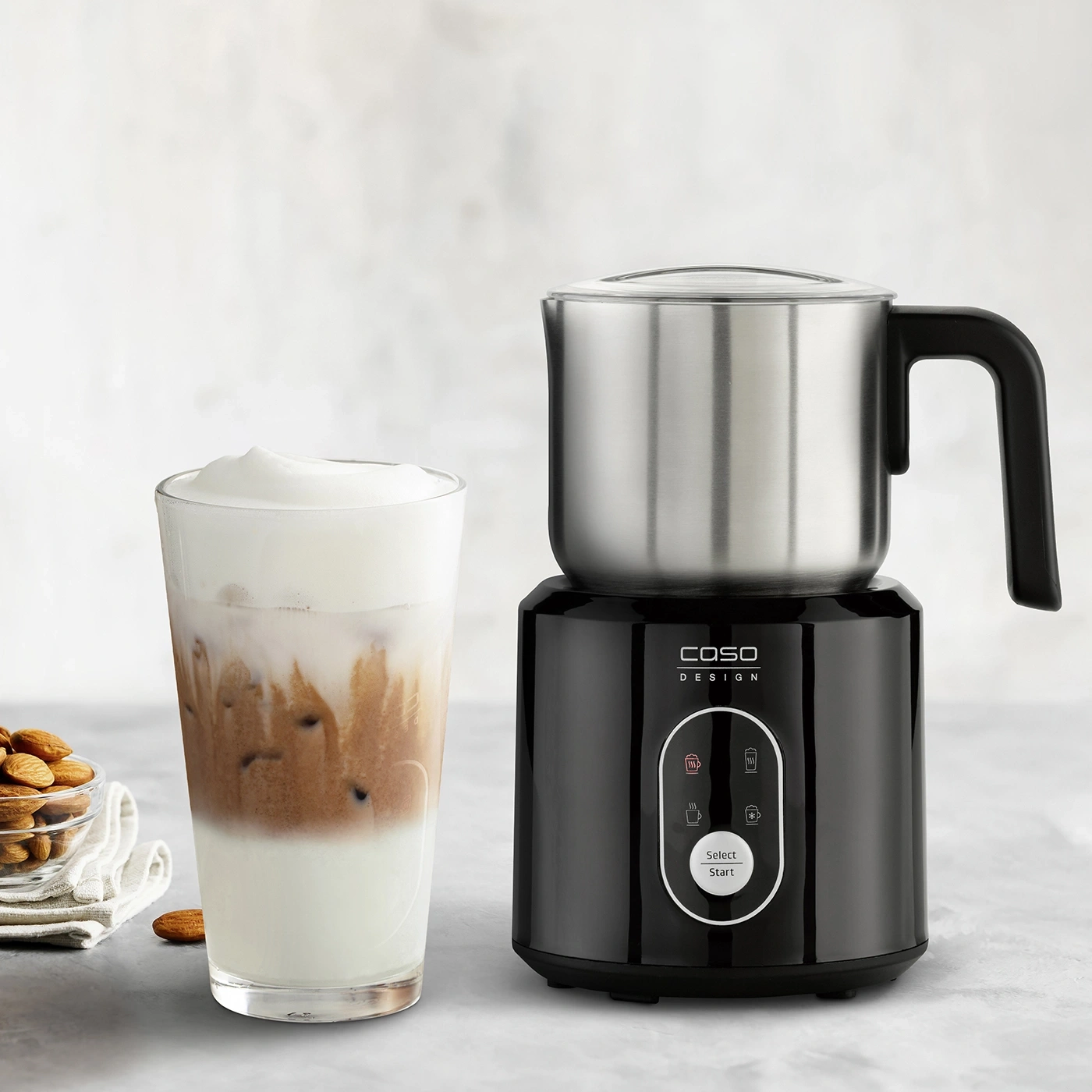 Milk frother with drink and almonds on a table