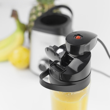 Nahaufnahme eines Mixers mit Obst im Hintergrund, Smoothie-Zubereitung