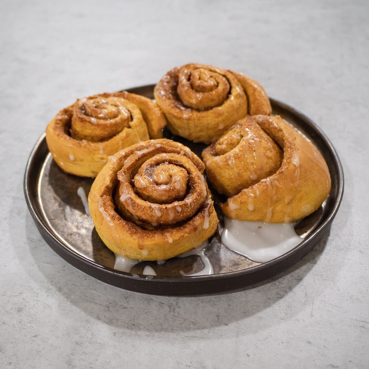 Close-up of four cinnamon rolls on a plate with icing dripping down.