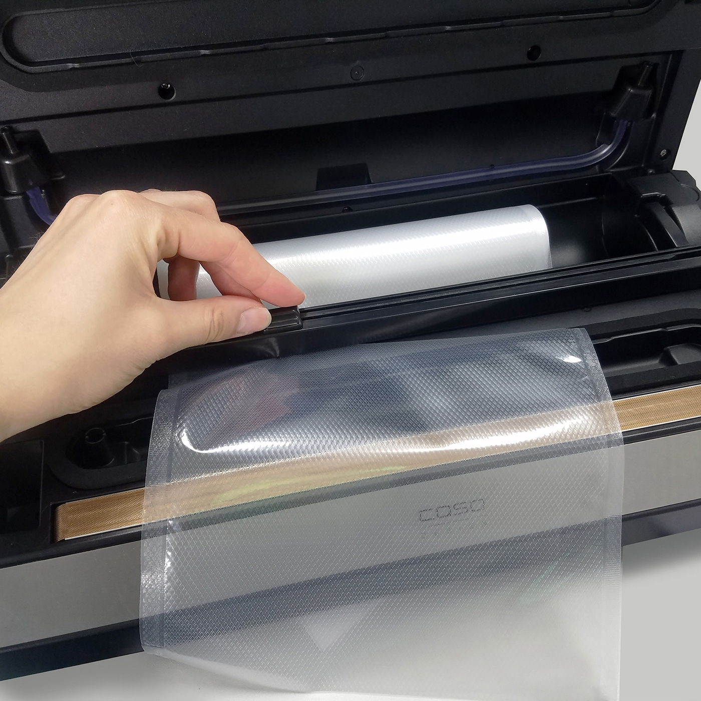 Person operating a vacuum sealer with a roll of film and a bag, close-up, detail shot