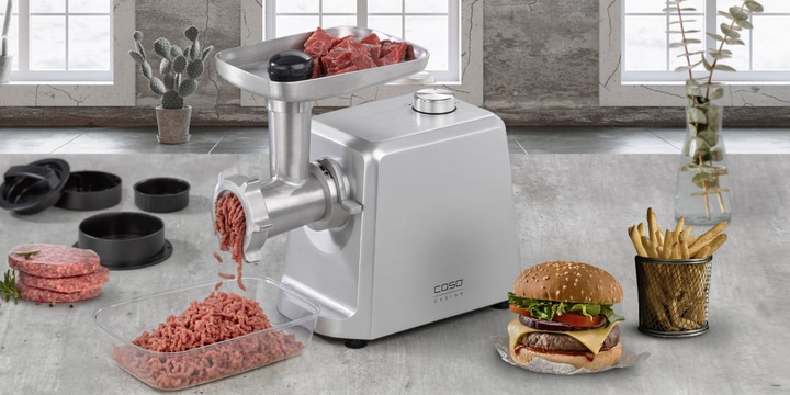 Meat grinder with burger, fries and ingredients on a table.