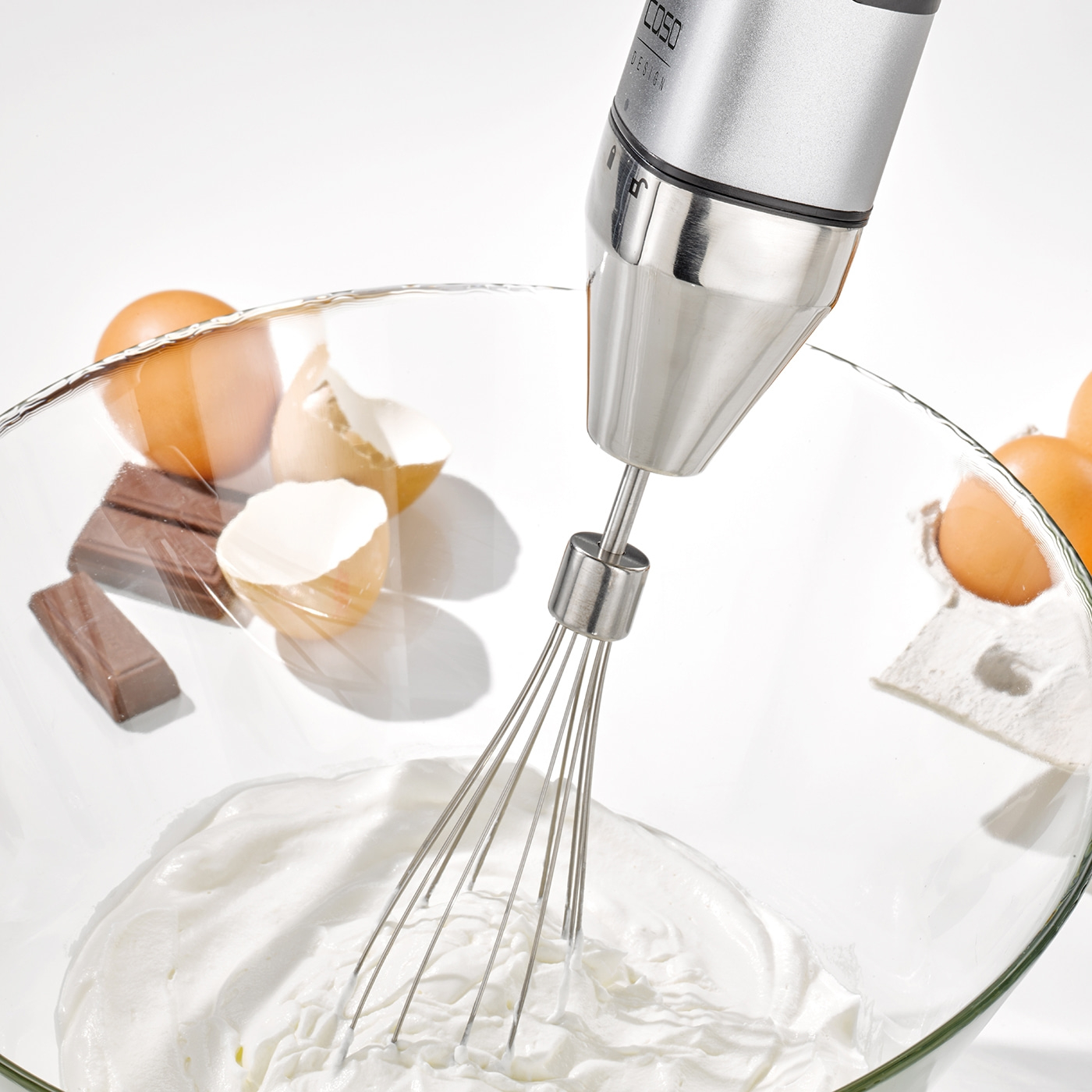 Hand mixer in a bowl with cream, eggs, and chocolate