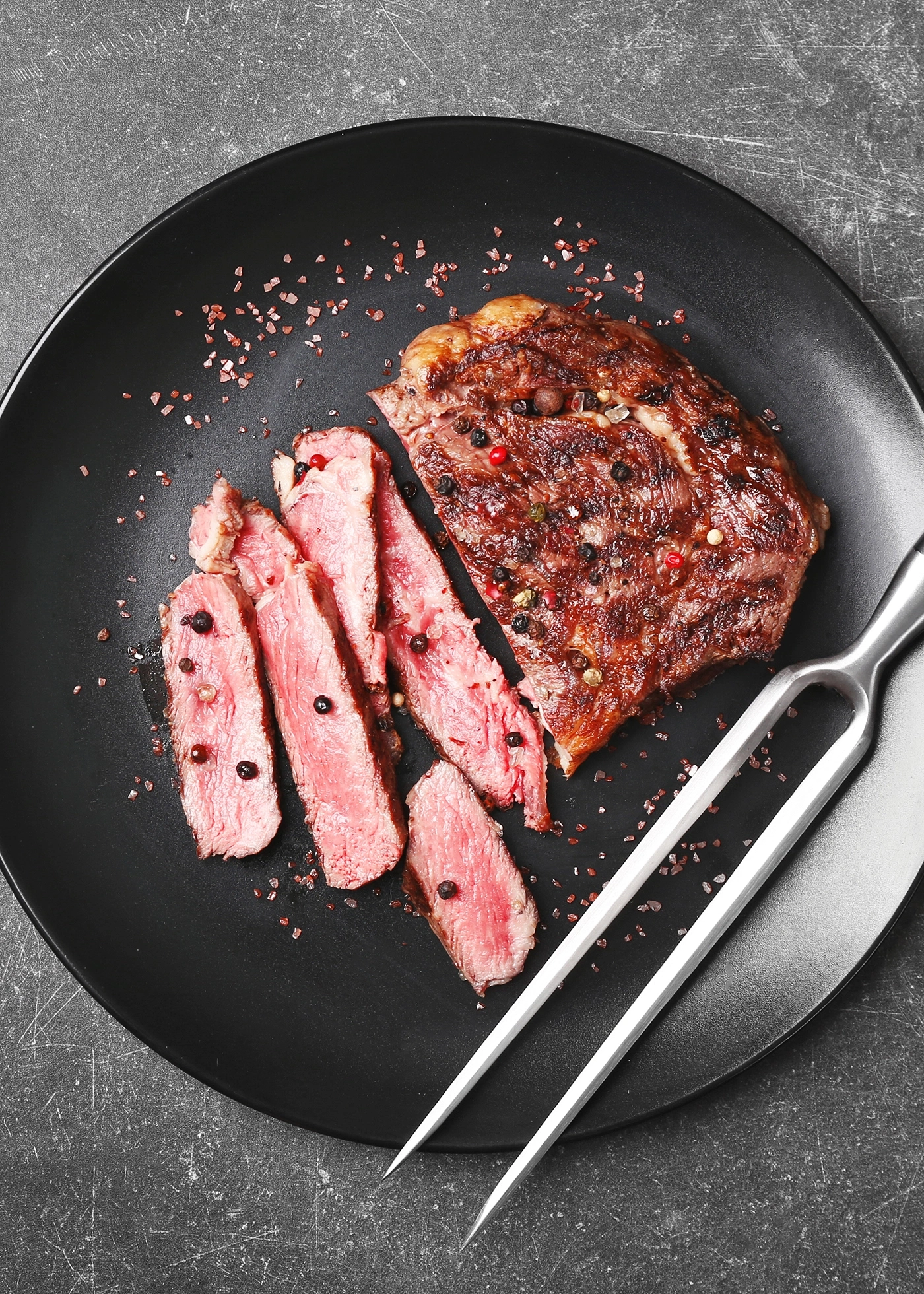 Pan-seared and sliced steak on black plate with seasoning