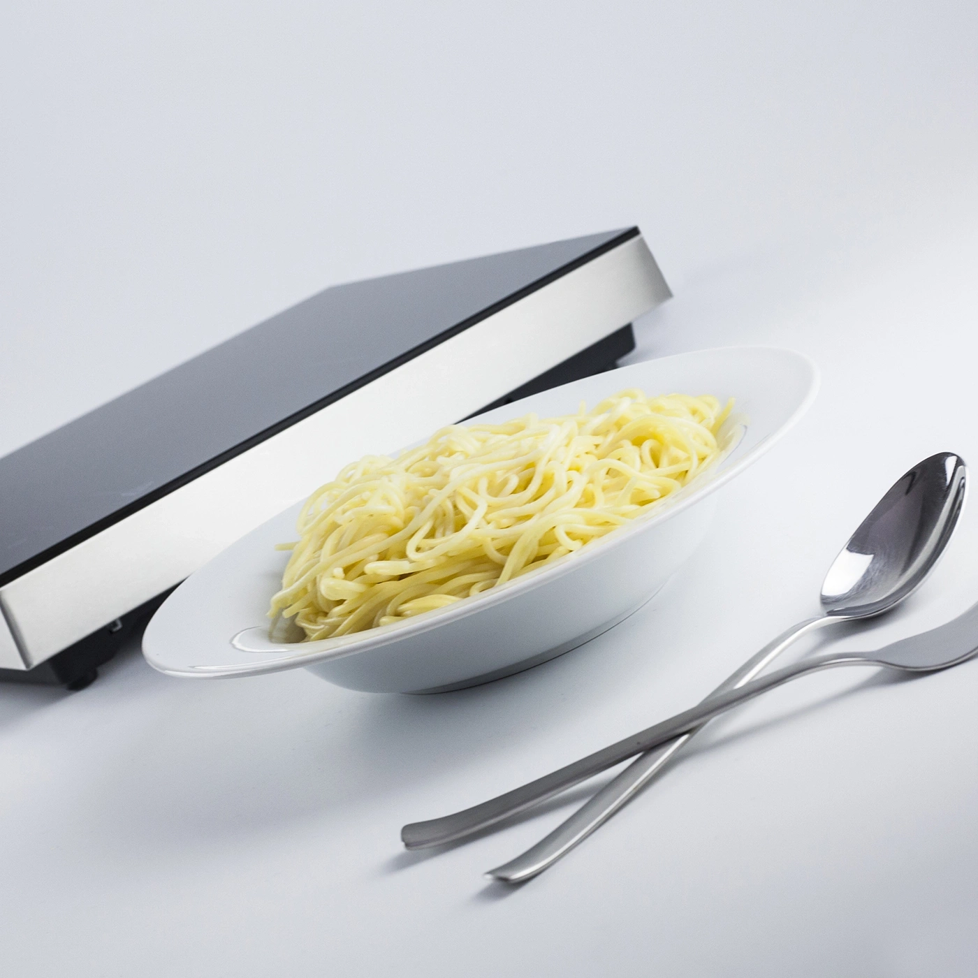 Teller mit Spaghetti, Gabel und Löffel, Kochfeld im Hintergrund