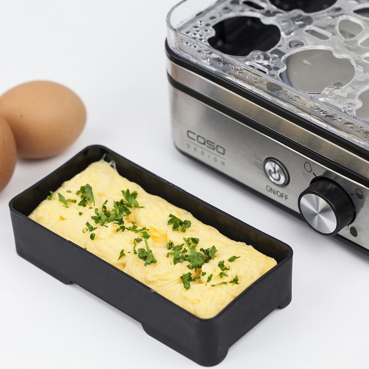 Egg dish in black form with egg cooker and eggs in the background