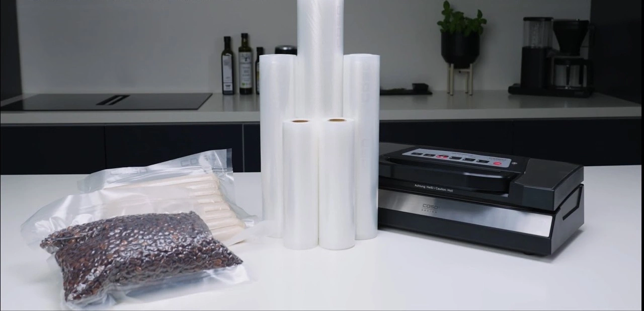 Vakuumiergerät mit Rollen und verpackten Lebensmitteln auf weißem Tisch