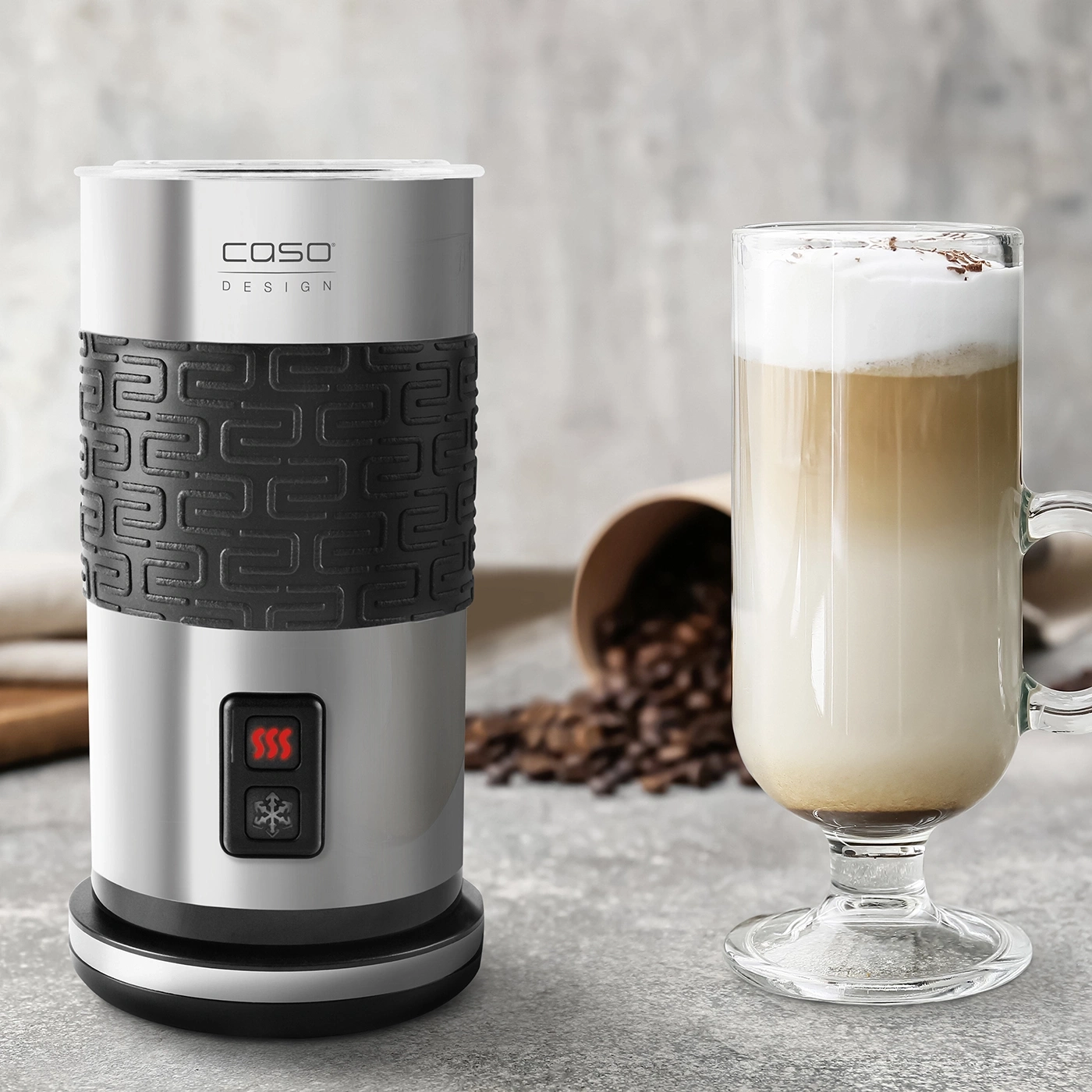 Milk frother and latte macchiato glass on gray surface with coffee beans