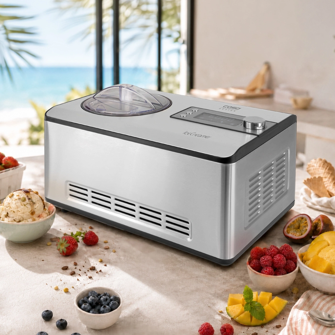 A silver ice cream maker sits on a counter with fruit, ice cream, and waffle cones.