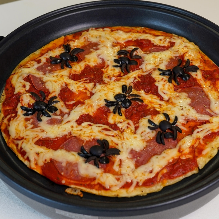 Halloween-Pizza mit Spinnen aus Oliven, auf einem schwarzen Teller, lecker.