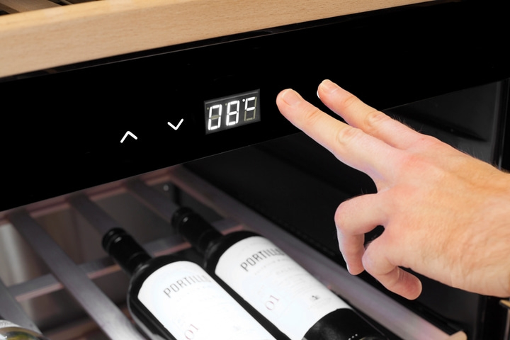 Weinkühler mit Temperaturanzeige und Bedienung durch Finger, Weinflaschen im Regal