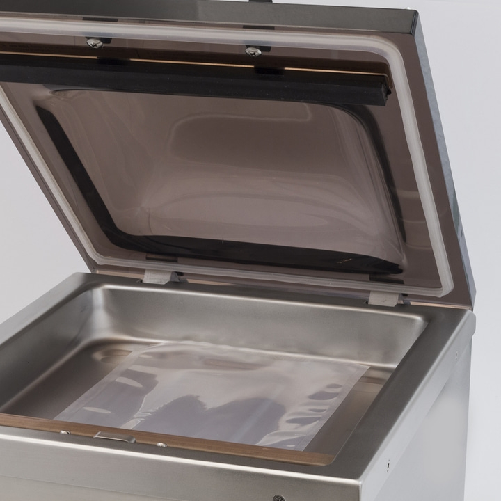 Vacuum sealer with open lid and plastic bag inside the chamber.