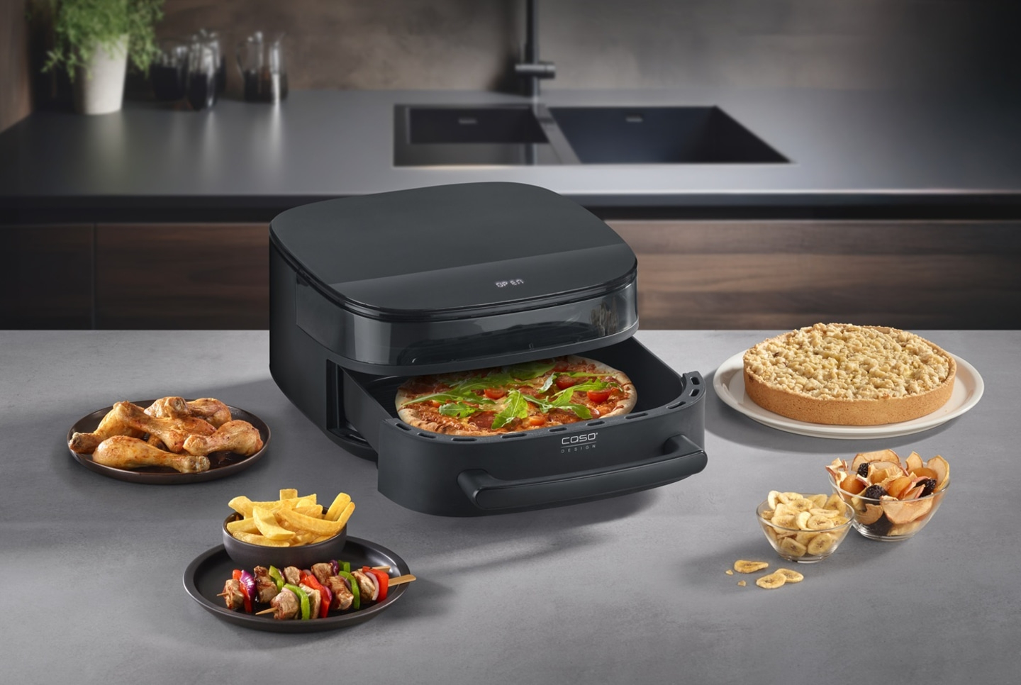 Ein schwarzer Heißluftfritteusen-Ofen mit Pizza, Hähnchenschenkeln, Spießen, Pommes und Kuchen.