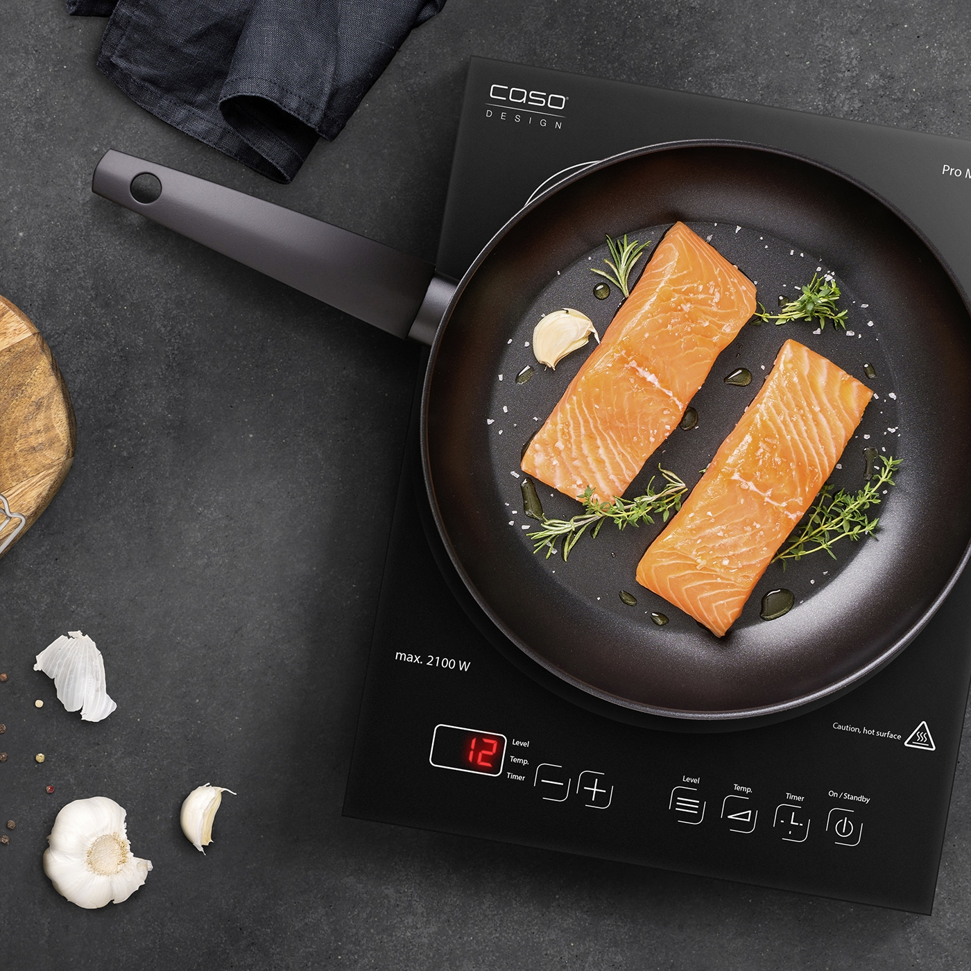 Induction cooktop with salmon in pan, garlic, herbs, black background, cooking, food preparation
