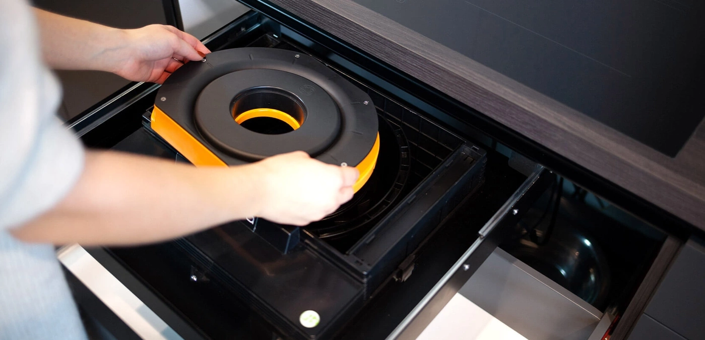 A person inserts a black and orange ring into a range hood system.