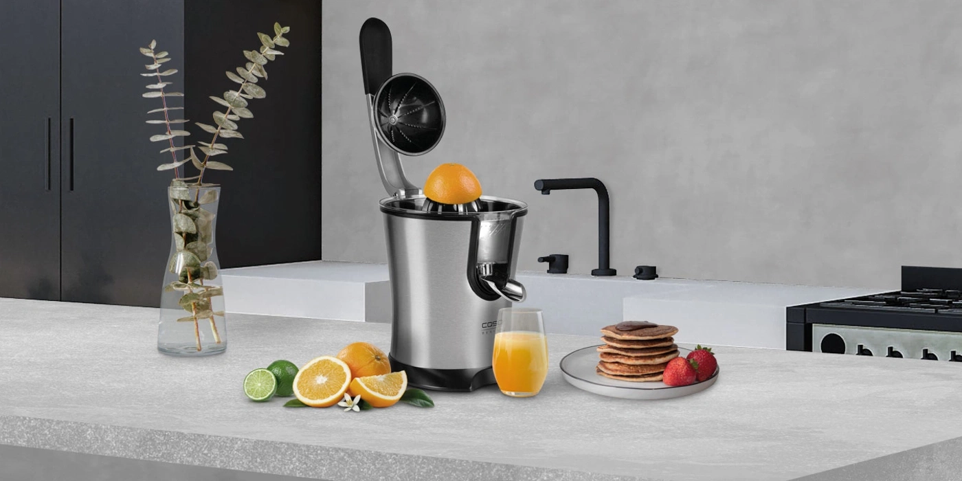 Küchenszene mit Saftpresse, Obst, Saft und Pfannkuchen
