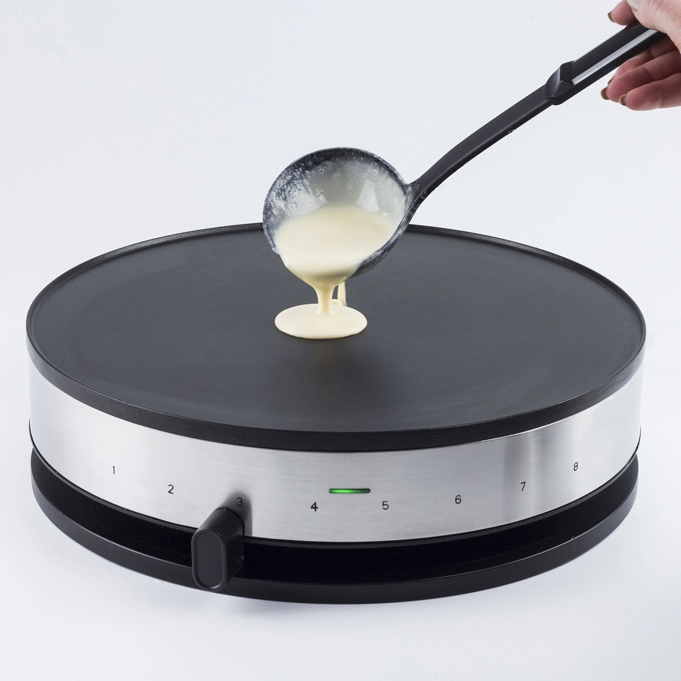 Pfannkuchenteig wird mit einer Kelle auf einer Crêpes-Maschine verteilt.