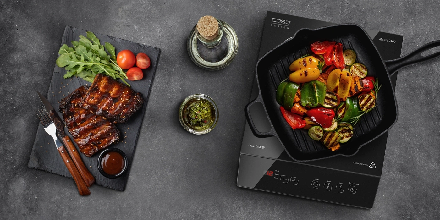 Gegrilltes Gemüse und Rippchen auf einem Tisch mit Soßen und Öl.