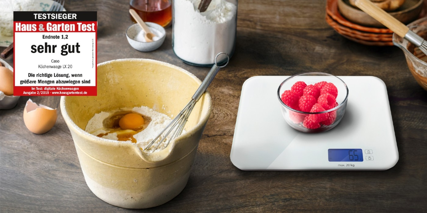Küchenwaage mit Himbeeren, Mehl, Eiern und Schneebesen auf Holzuntergrund. Sehr gut getestet.