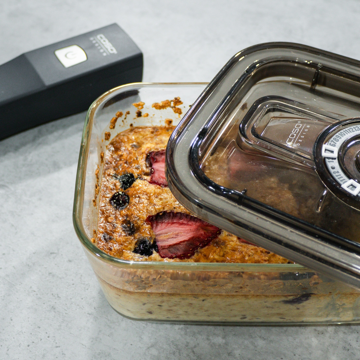 Glass container with food, lid, strawberries and blueberries, gray background