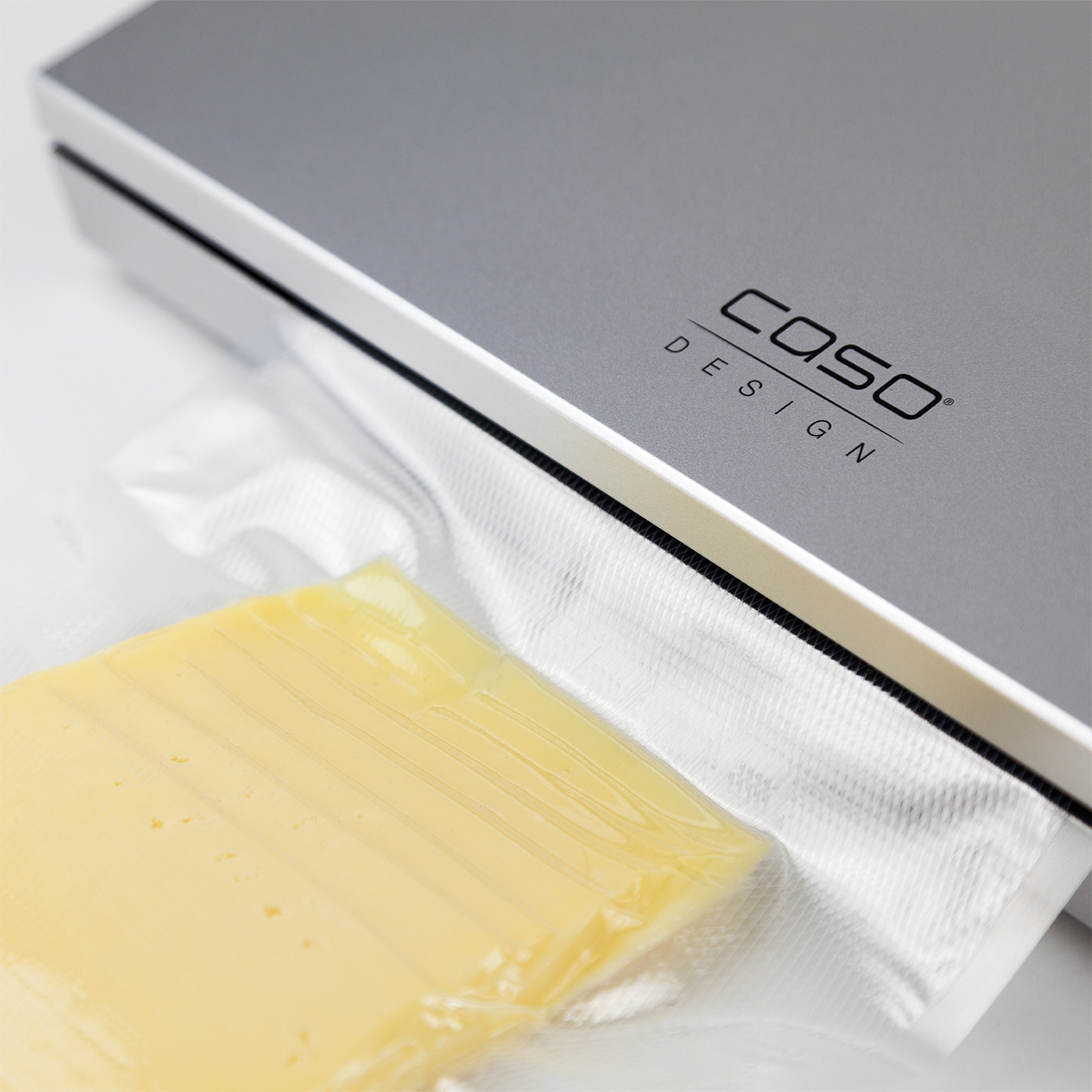 Cheese in vacuum packaging next to Caso Design device, gray and white.