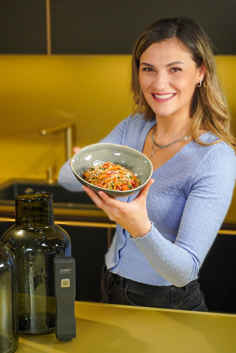Woman holding food bowl smiles in kitchen with golden background.