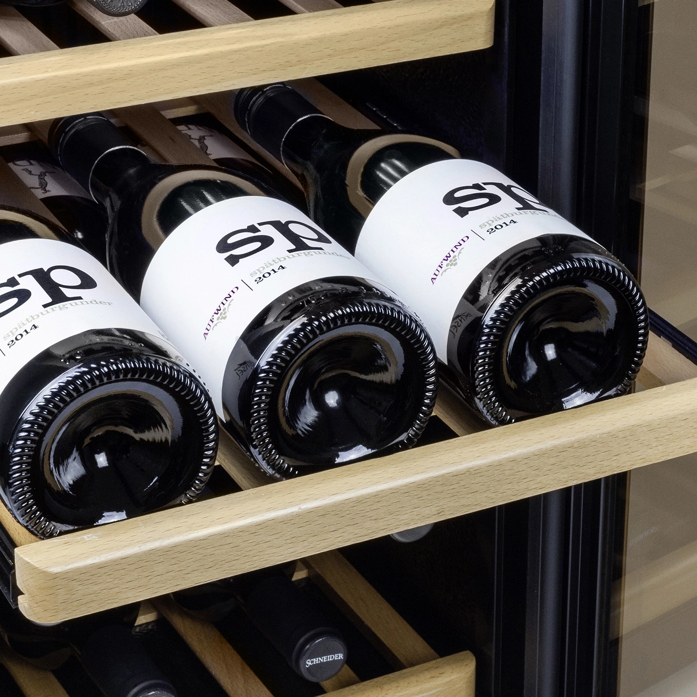 Wine bottles in a wine cooler, with labels, wooden shelves, and a black background.