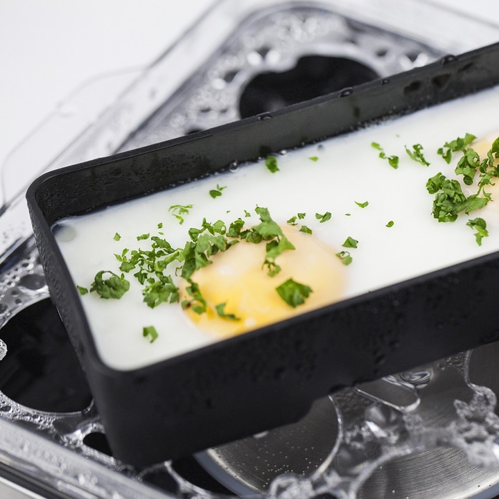 Eggs in a black container with parsley. Close-up shot of food, white sauce.