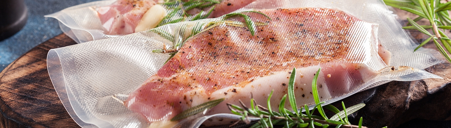 Vakuumverpacktes Fleisch mit Kräutern auf einem Holzbrett, Nahaufnahme