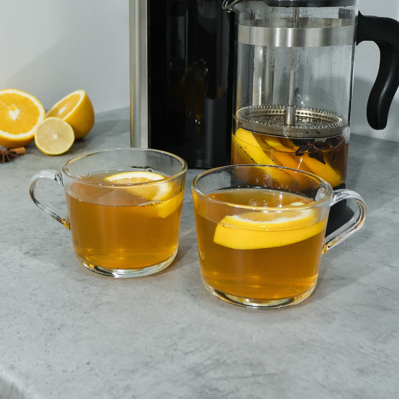 Two cups of tea with lemon, a teapot, and some lemons in the background.