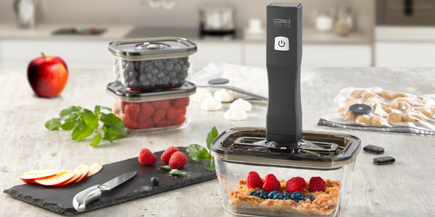 Fruits, containers, and a vacuum sealer on a kitchen table setting.