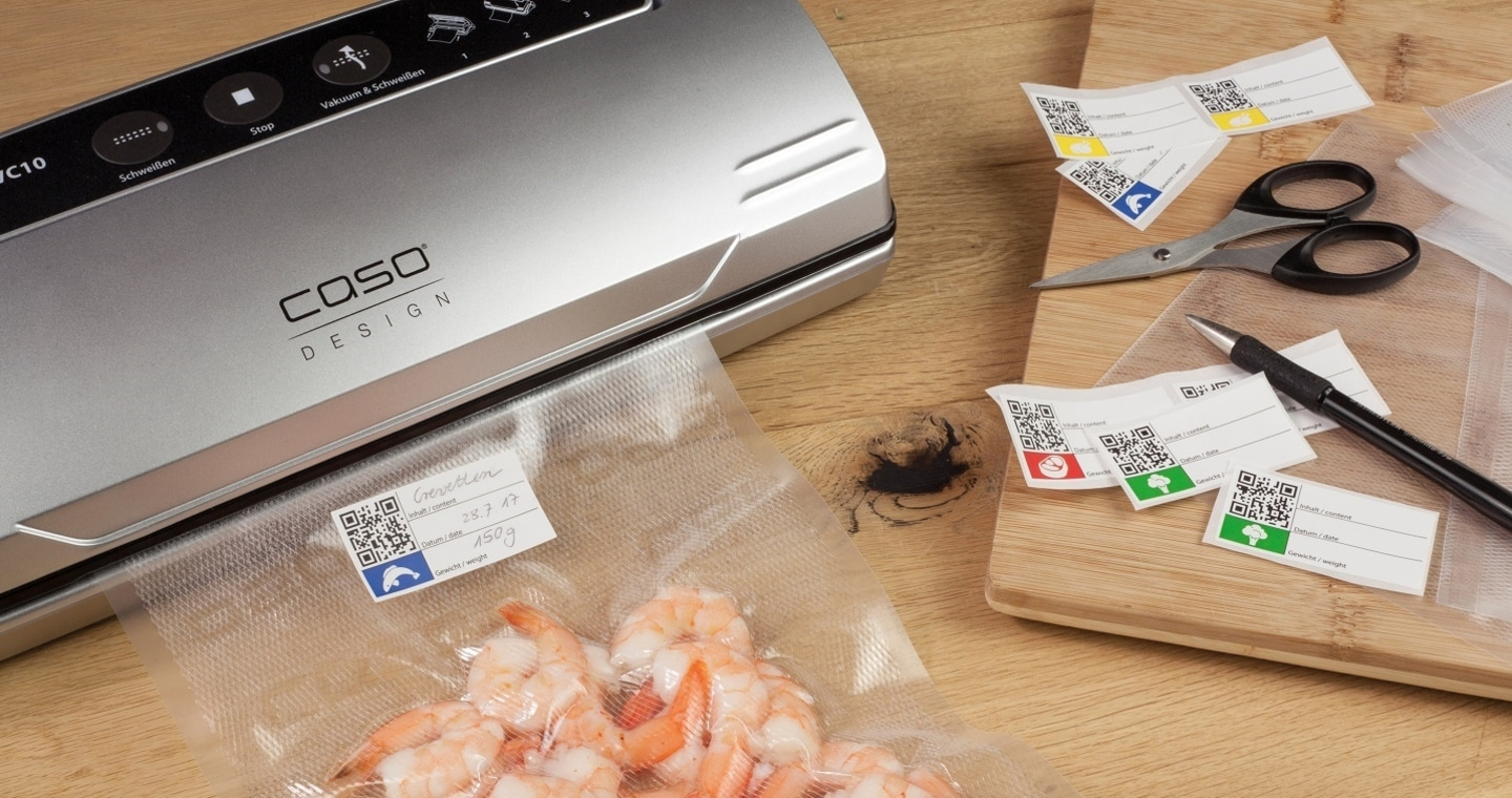 Vacuum sealer with shrimp, labels, and accessories on a wooden board.